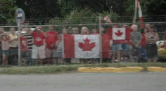 Des gens avec des drapeaux canadiens le long de l'autoroute